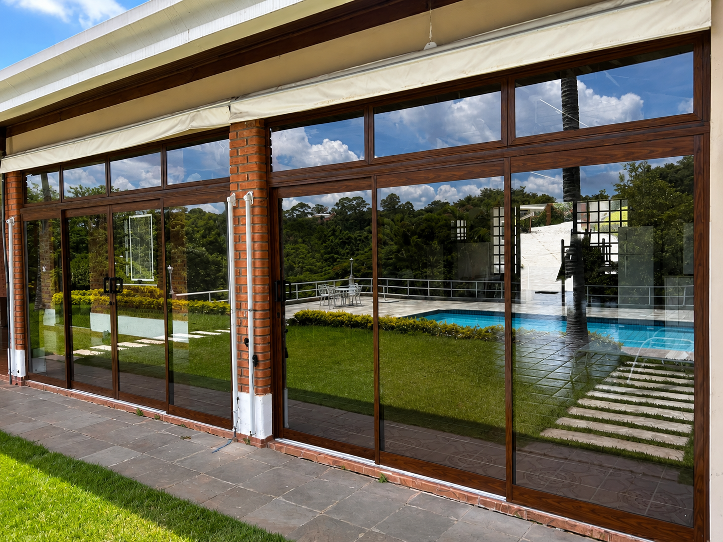 Fechamento em vidro com esquadrias amadeiradas integrando varanda e piscina